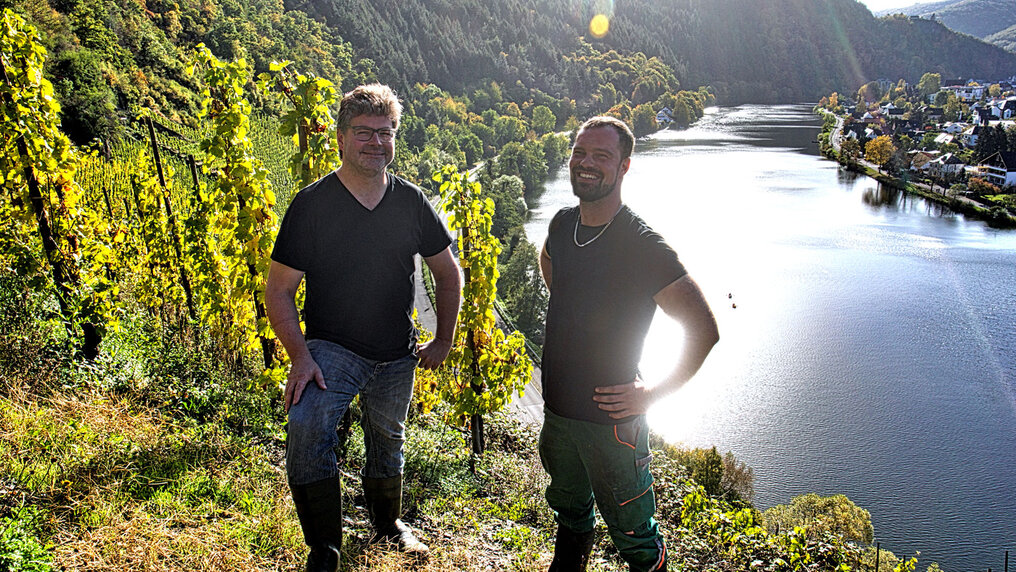 Gernot Kollmann und Philipp Clementi stehen im Weinberg mit Blick auf die Mosel