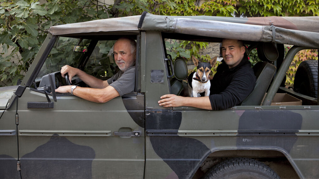 Friedrich Senior and Fritz Junior with their dog sitting in their Jeep, looking at the camera