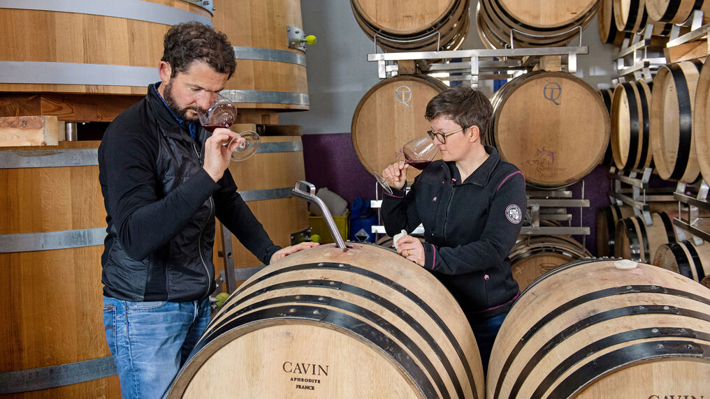Sina and Matthias Gubler-Möhr take barrel samples in their cellar. Both bring the glass containing the red wine sample to their noses.