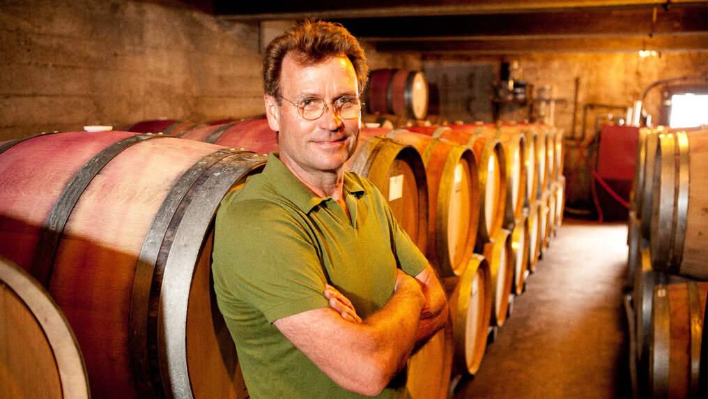Winemaker Jeffrey Patterson leans with his arms crossed against a wooden barrel in the Mount Eden wine cellar.