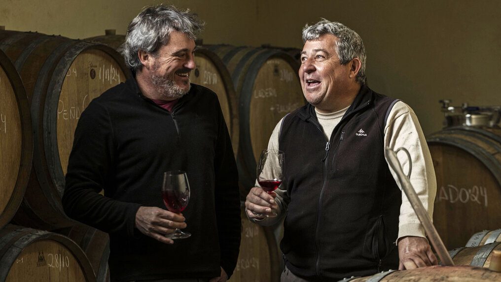 Marc Isart and Miguel Santiago Carillo chat in the wine cellar over a glass of red wine.
